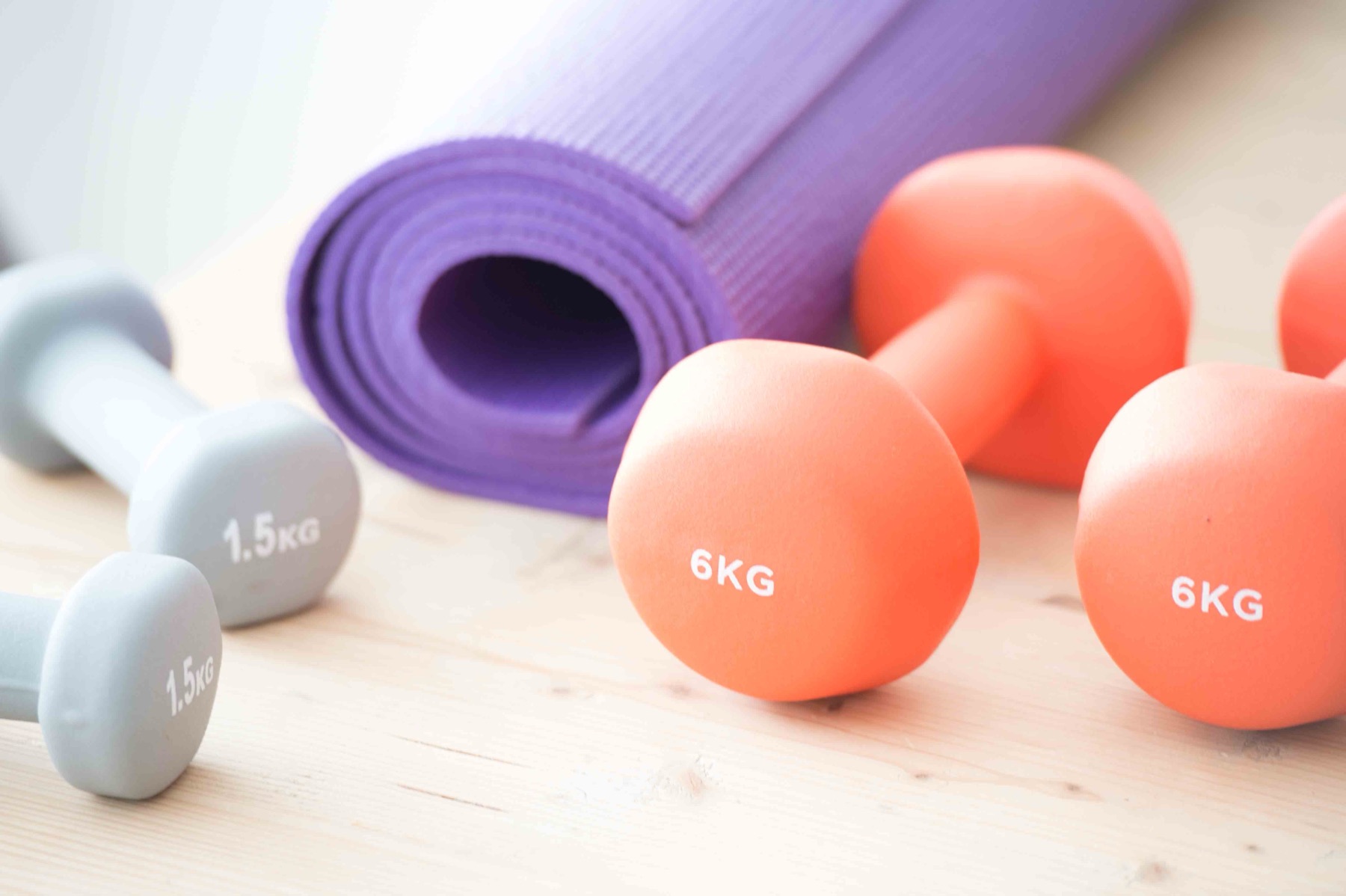 Coral and grey dumbbells beside a rolled purple exercise mat on a wooden floor