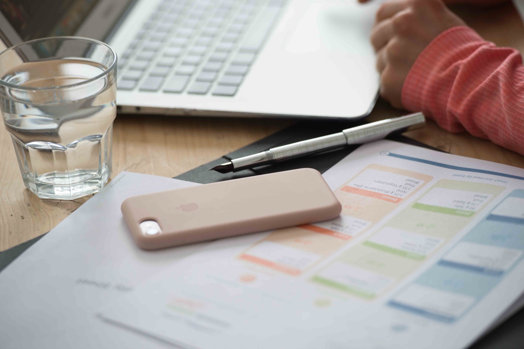 A printed training plan on a wooden desk with a fountain pen, a phone and a glass of water